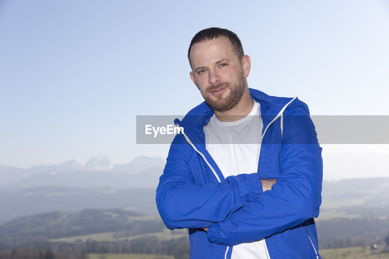 Portrait of man with arms crossed standing against sky