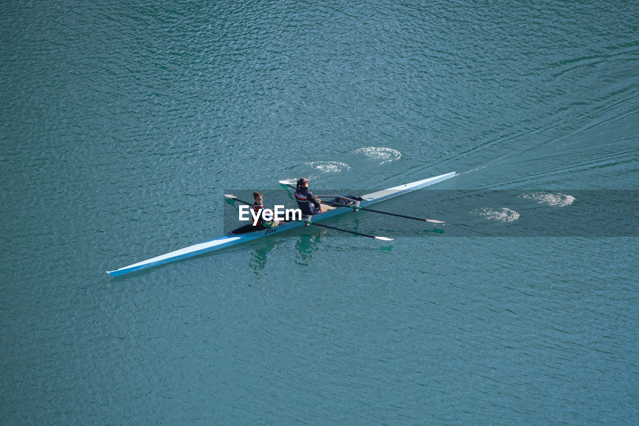 water, rowing, nautical vessel, transportation, high angle view, sports, teamwork, oar, cooperation, men, nature, mode of transportation, day, togetherness, group of people, sculling, competition, water sports, sport rowing, adult, lifestyles, blue, waterfront, outdoors, rowboat, boating, leisure activity, lake, vehicle, motion, athlete, beauty in nature, boats and boating--equipment and supplies, boat, paddle, competitive sport