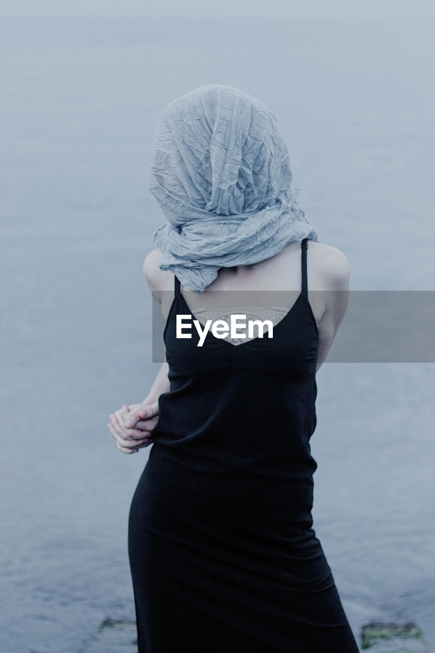 Woman covering face with scarf while standing by sea