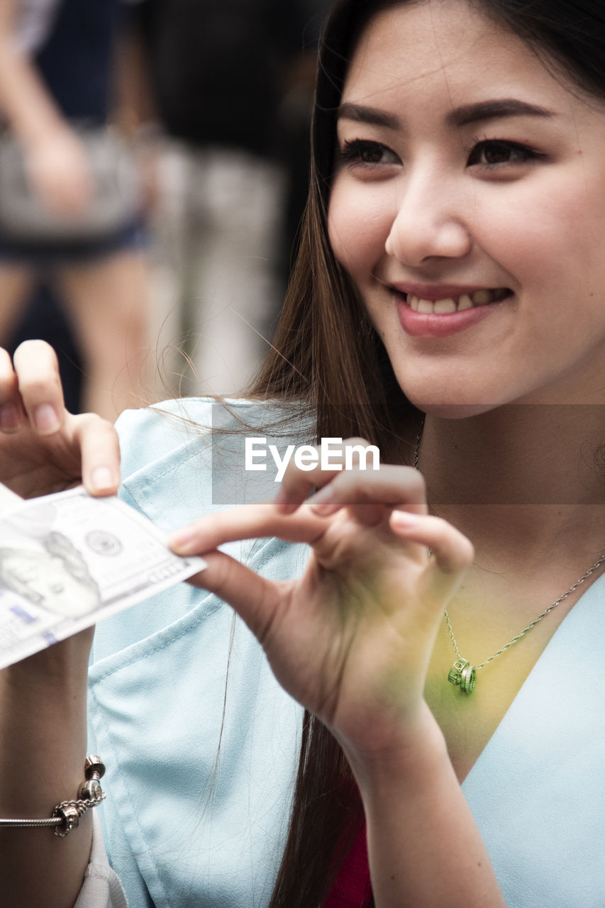 Smiling woman holding paper currency in city