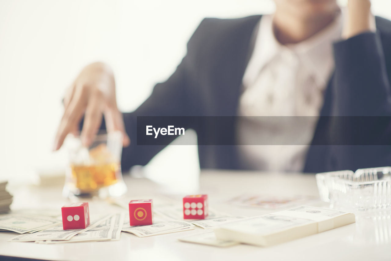 Midsection of businessman holding drink with dice and money on table