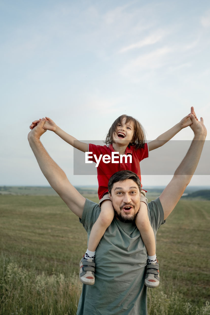 Cheerful father carrying son on shoulders and enjoying at field