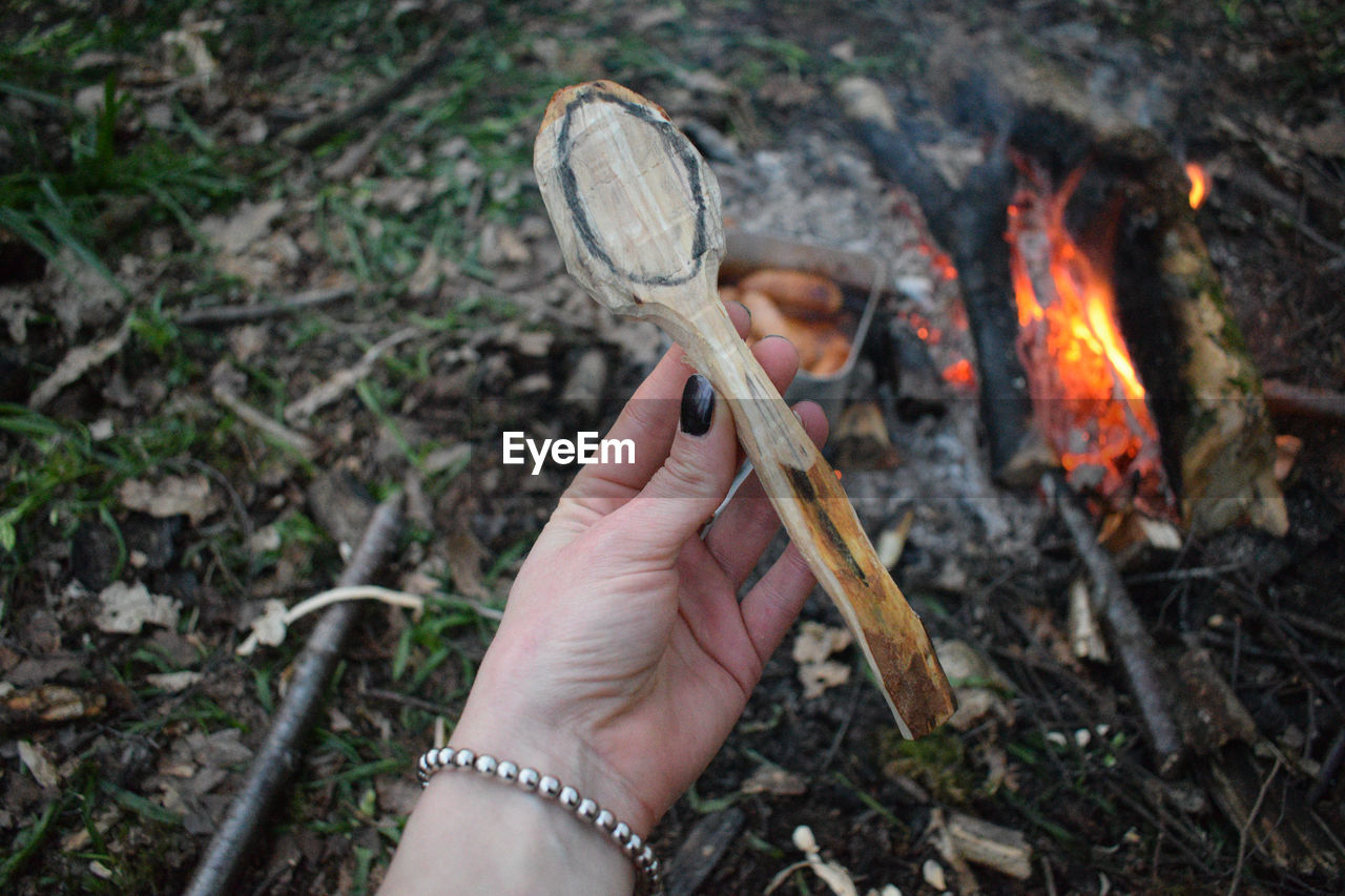 Cropped hand of woman holding wood over fire