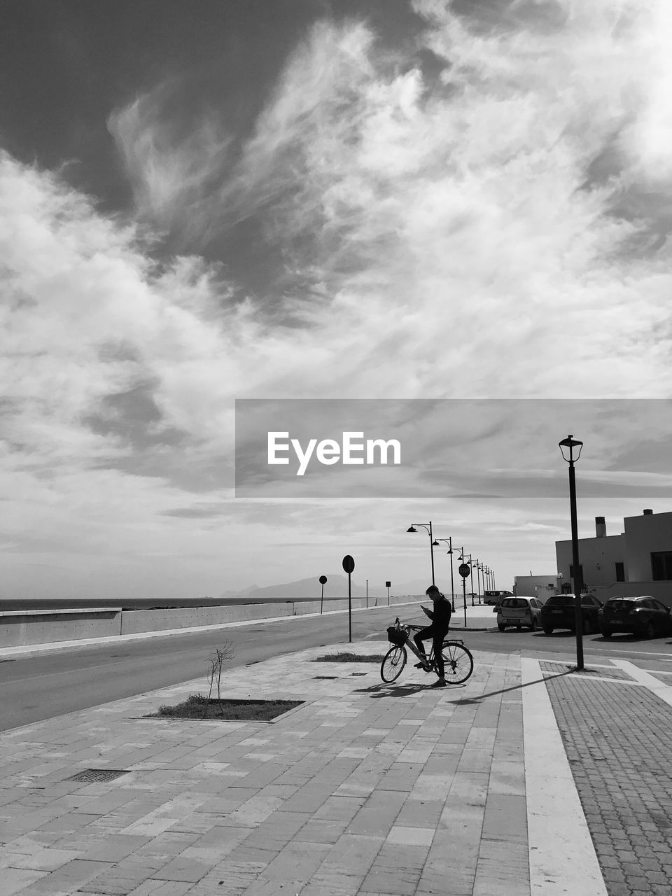 WOMAN ON BICYCLE BY STREET AGAINST SKY