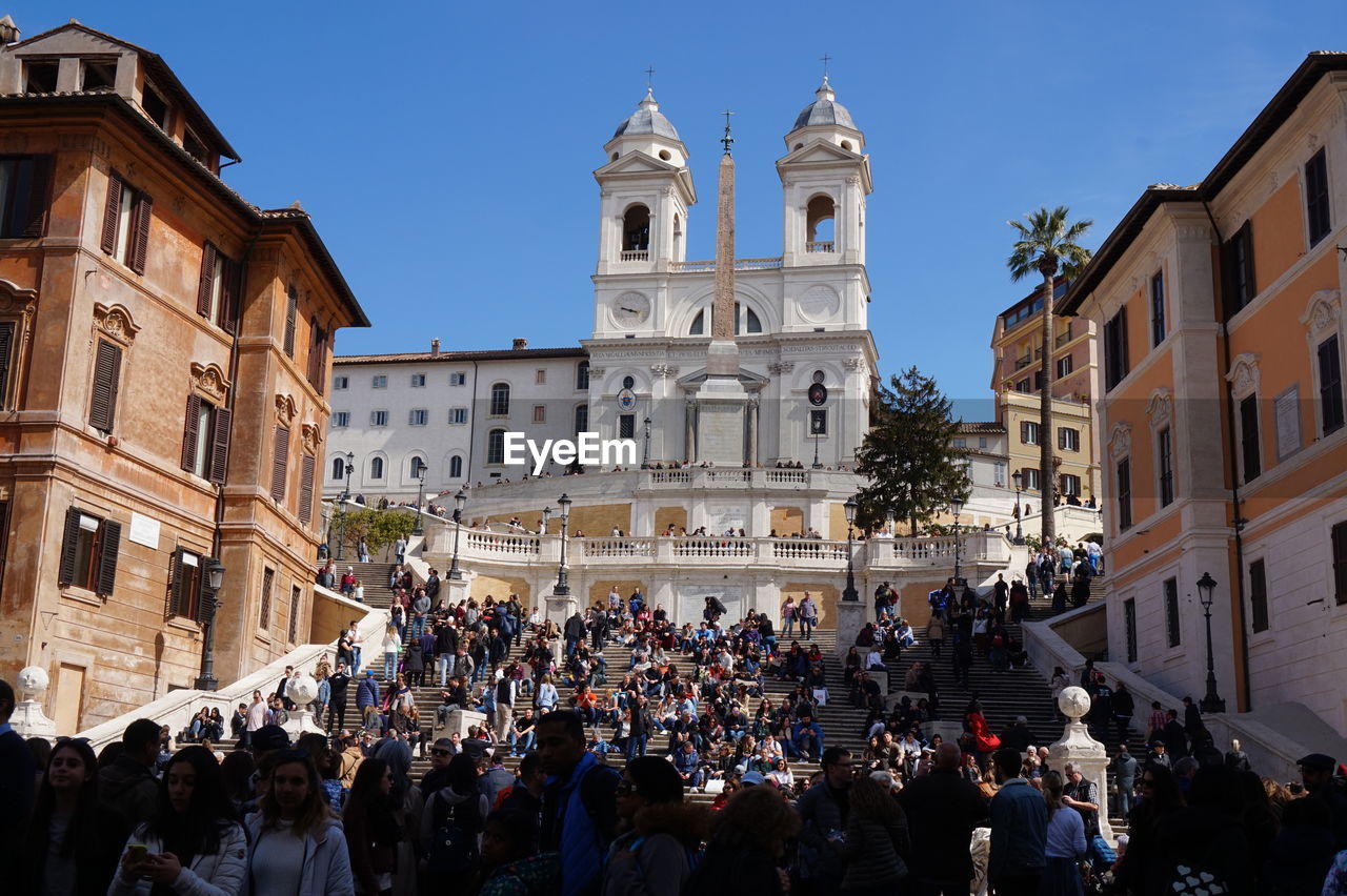 architecture, building exterior, crowd, built structure, large group of people, group of people, city, travel destinations, religion, building, tourism, town square, place of worship, nature, belief, sky, spirituality, travel, celebration, history, street, the past, men, town, outdoors, women, catholicism, tower, adult