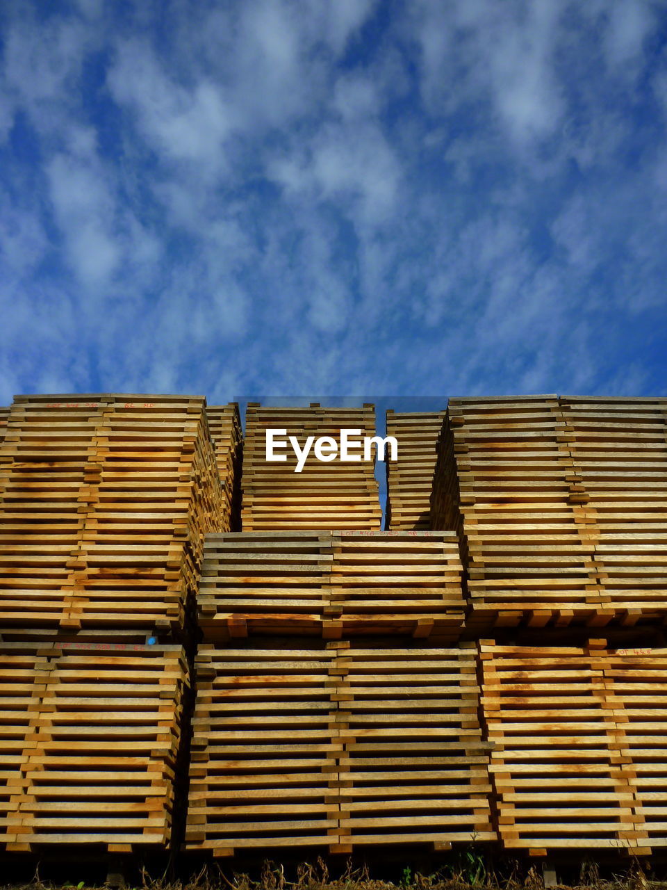 Low angle view of planks at lumber industry against cloudy blue sky