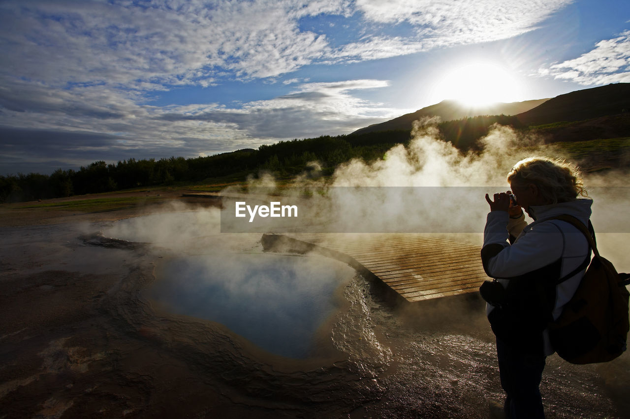 Mature woman taking picture of geothermal pool in iceland