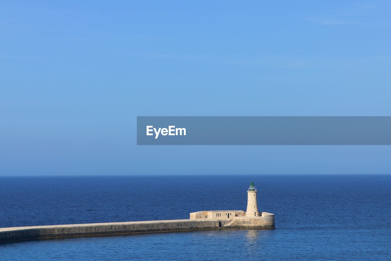 Scenic view of a breakwater and lighthouse on the mediterranean sea against a clear blue sky