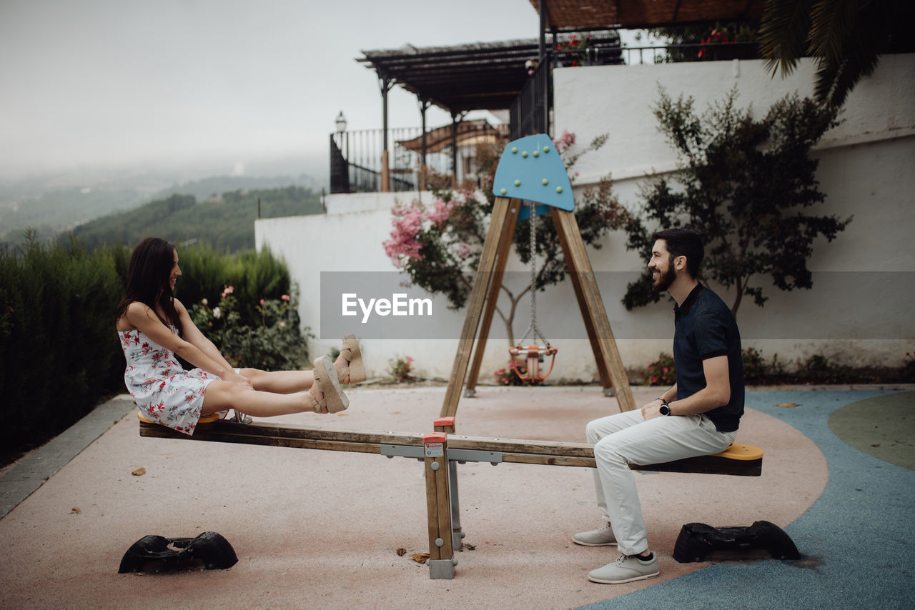 Side view of carefree couple swinging on seesaw on playground in country town at scenic mountain valley