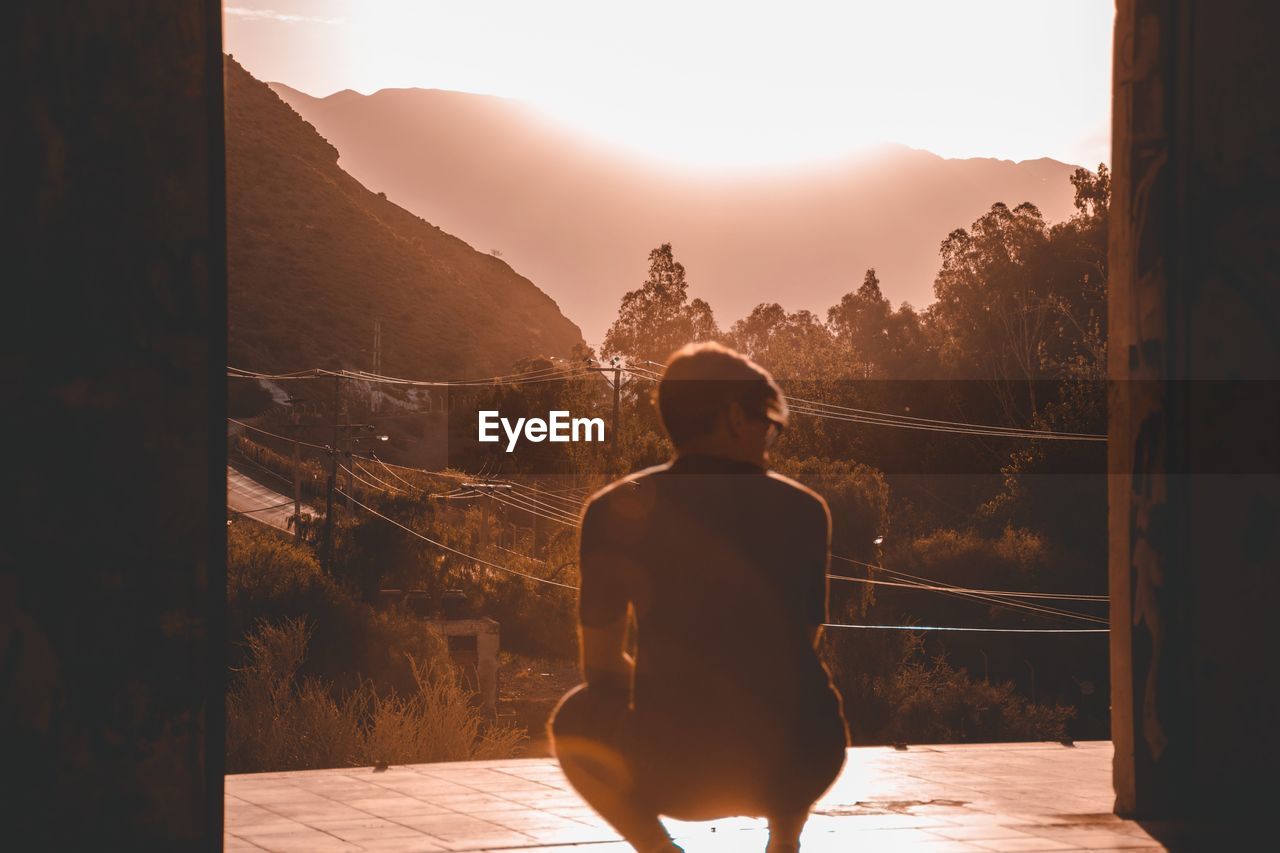 Rear view of man crouching on floor against mountains