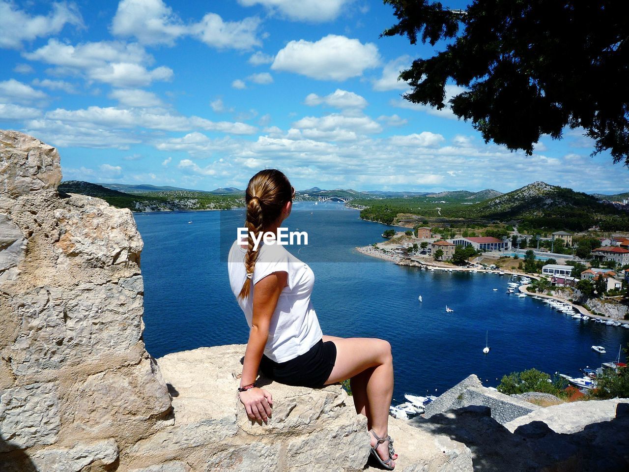 Woman looking at view while sitting on rock by sea against sky