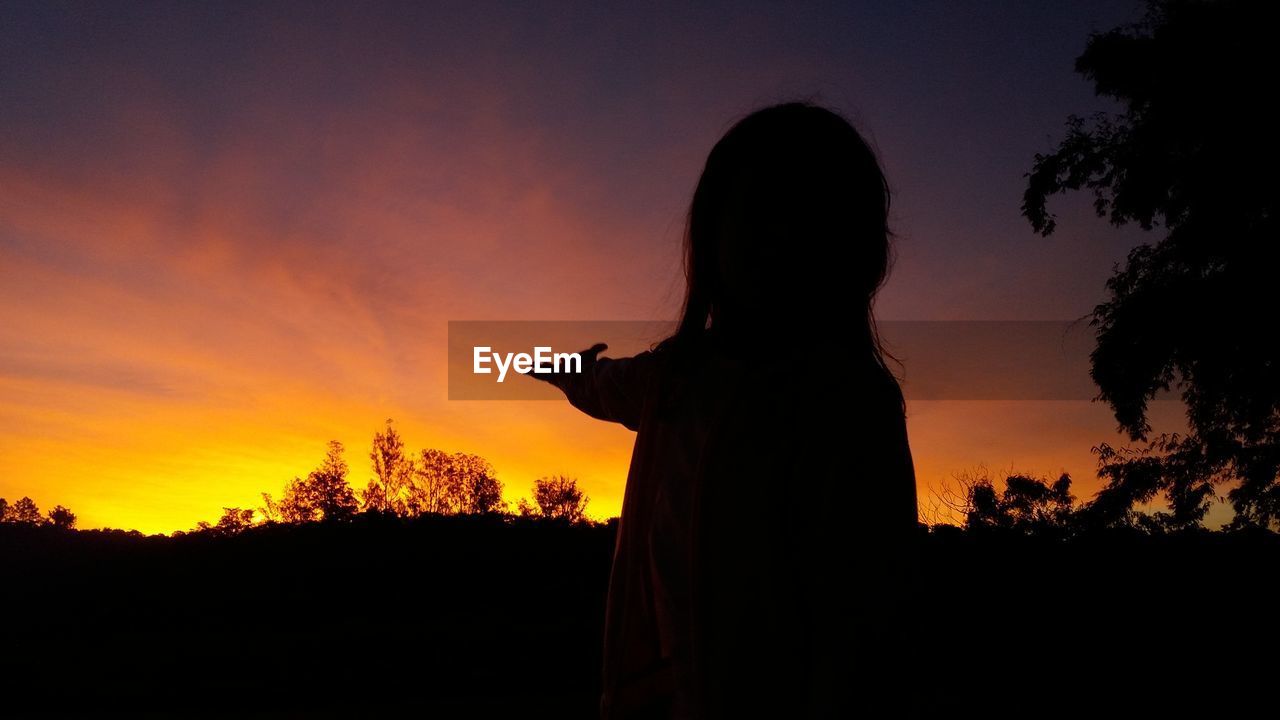 Woman gesturing on field against sky during sunset