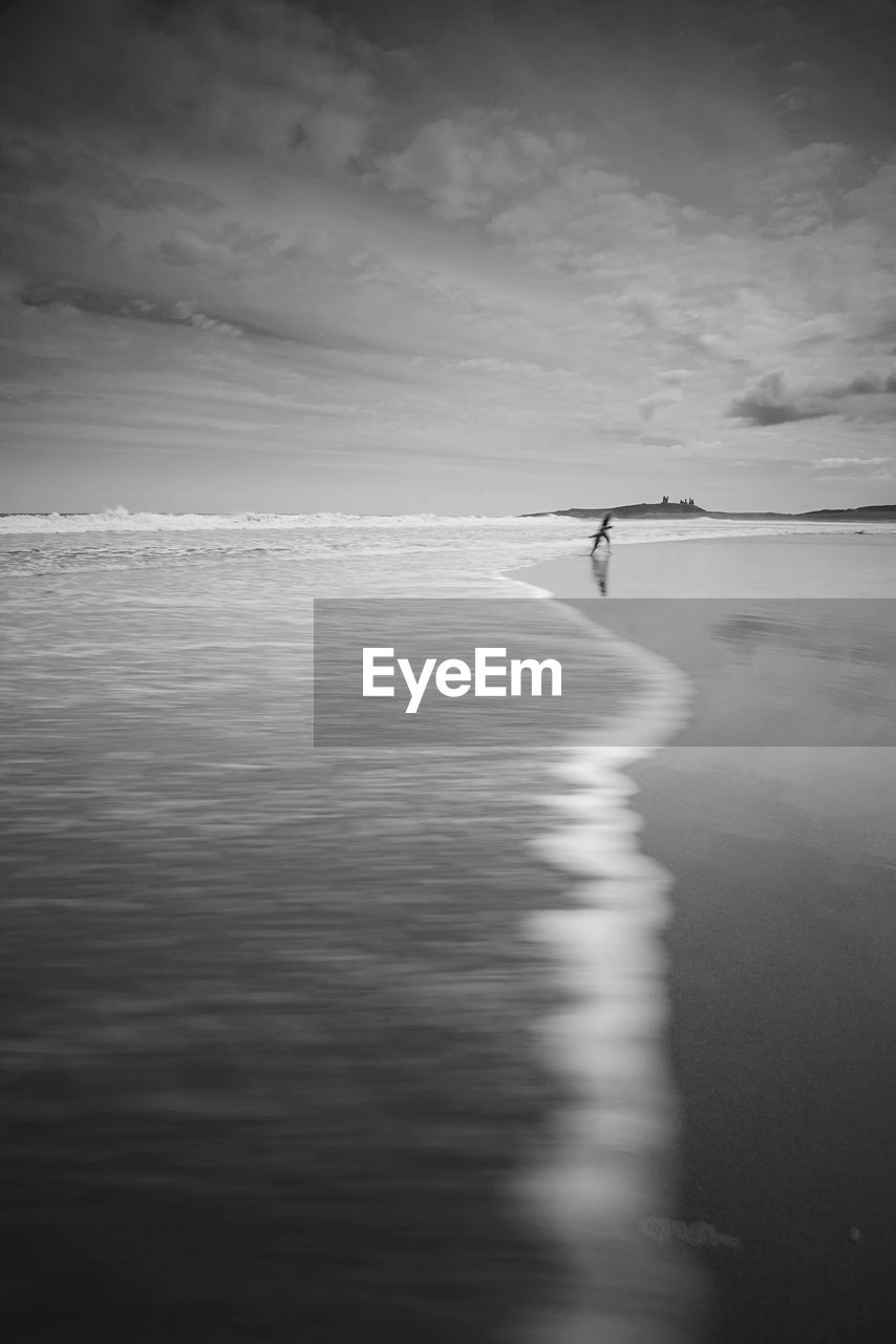 Person running on shore at beach against sky