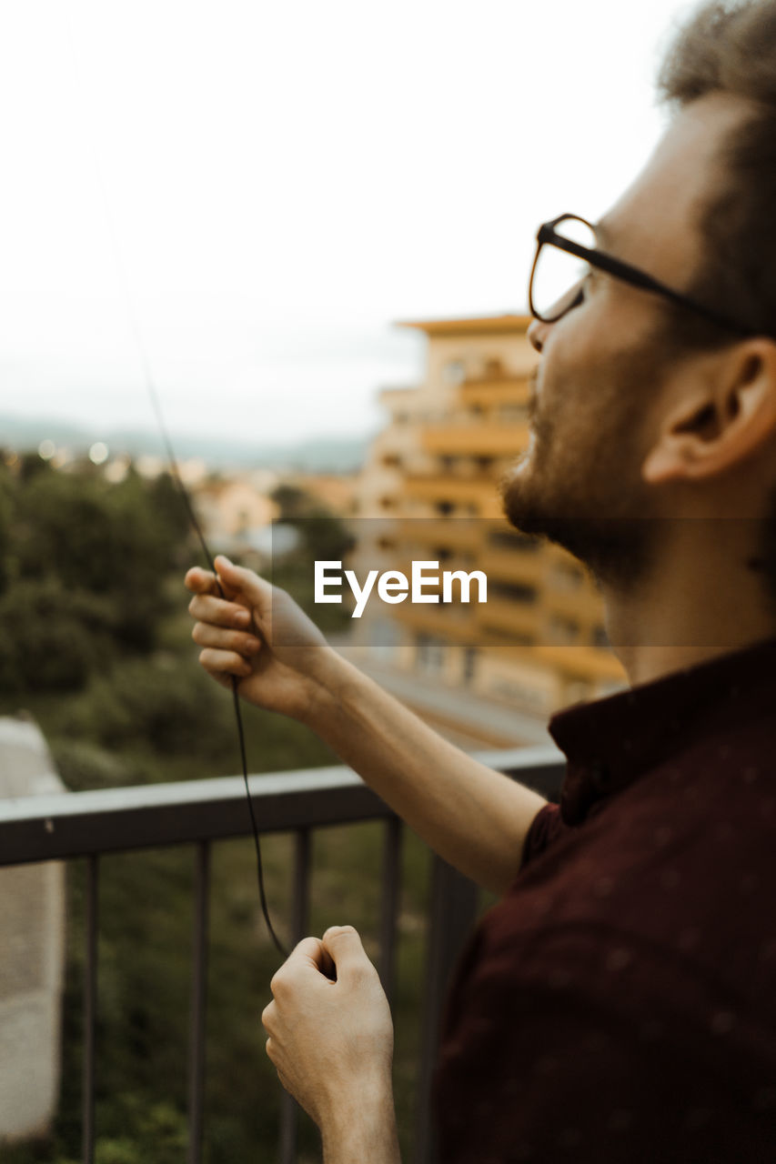 Young man with glasses trying to fly kite from his balcony.