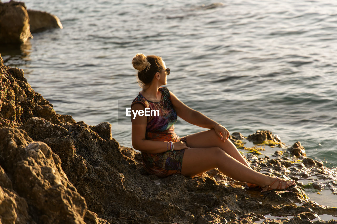 Side view of woman sitting on rock at beach