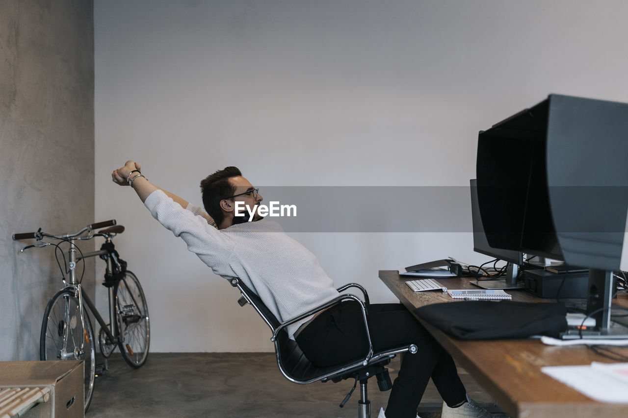 Young male hacker stretching hands while working on computer in startup company