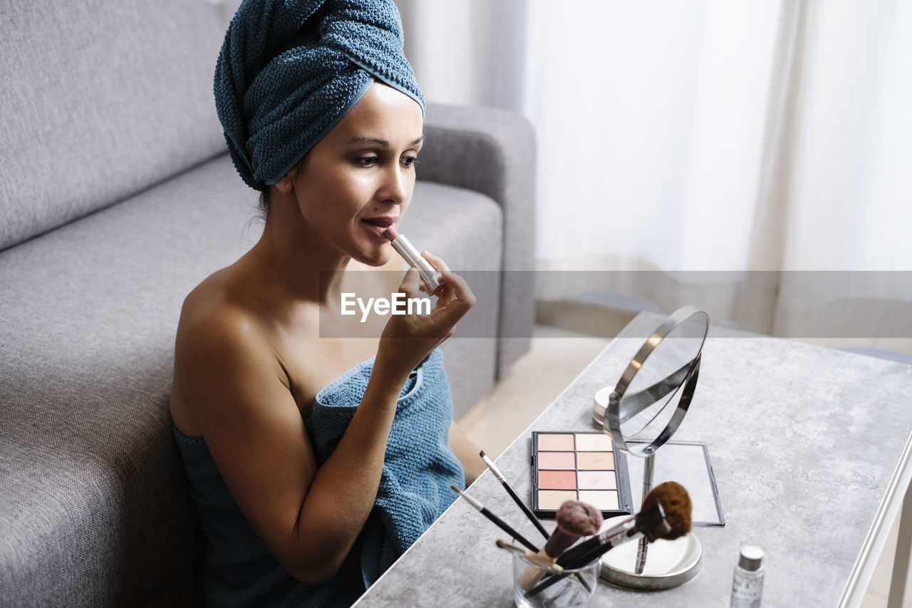 Side view of female applying natural colored lipstick during morning beauty routine