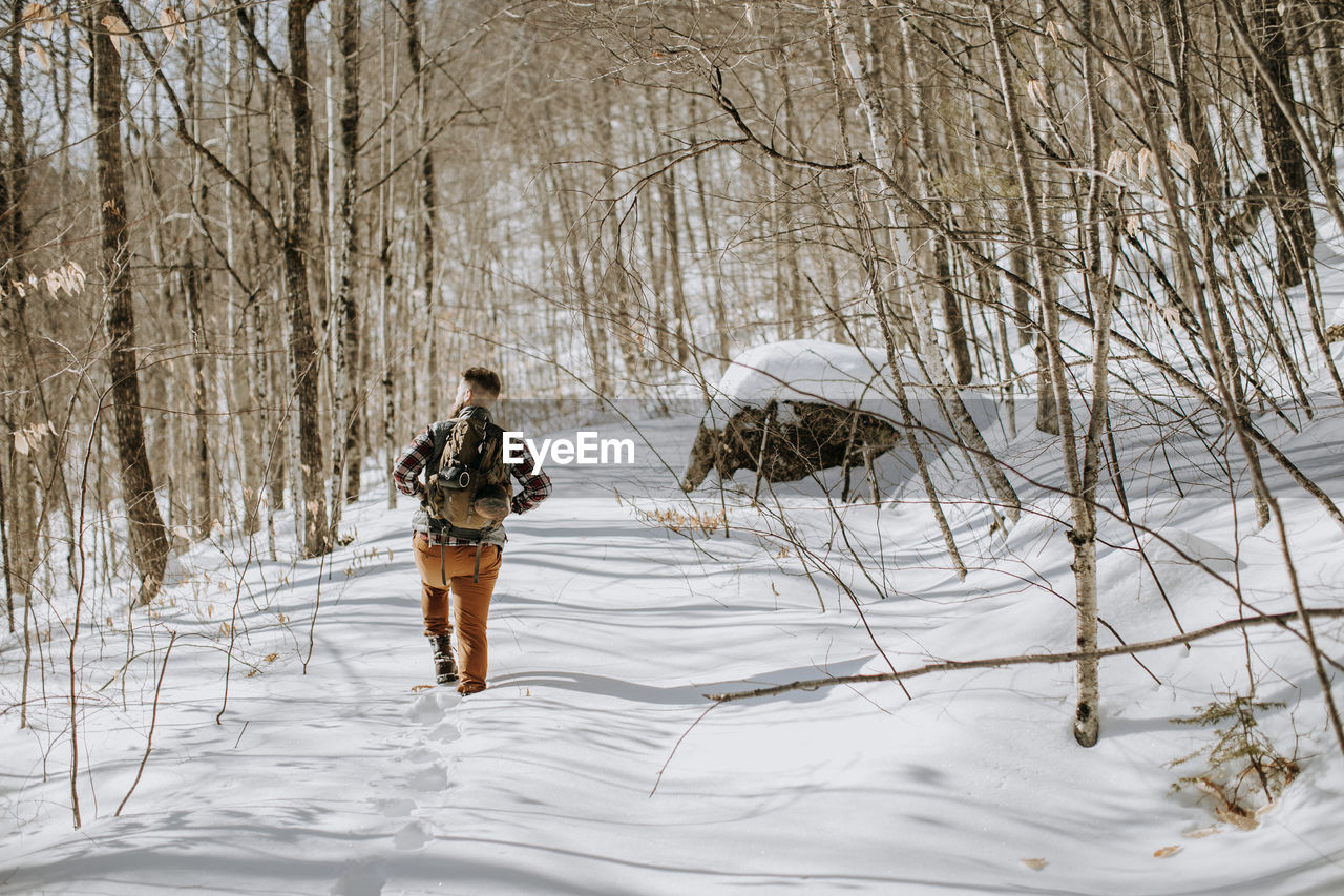 Man wearing pack walks and hikes through snow covered trees and woods