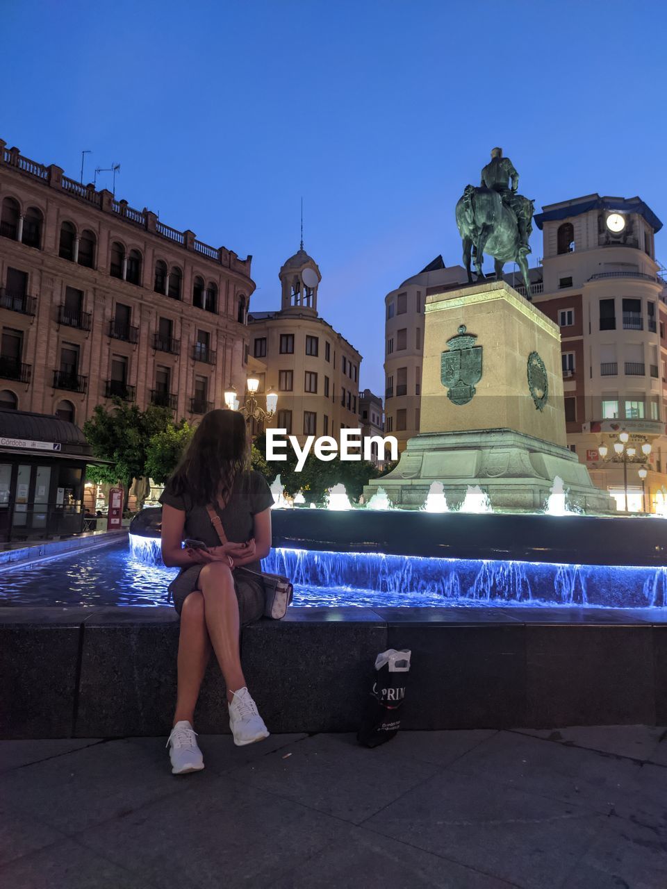 FULL LENGTH OF WOMAN SITTING OUTSIDE BUILDING AGAINST SKY