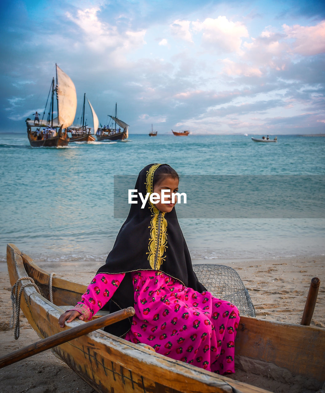 WOMAN SITTING BY SEA AGAINST SKY AT BEACH