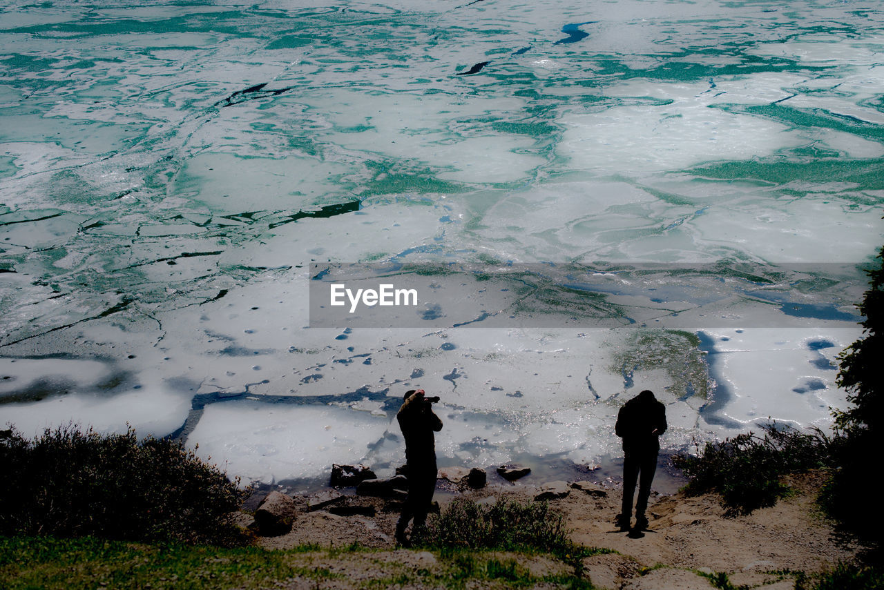 PEOPLE STANDING BY LAKE AGAINST SKY