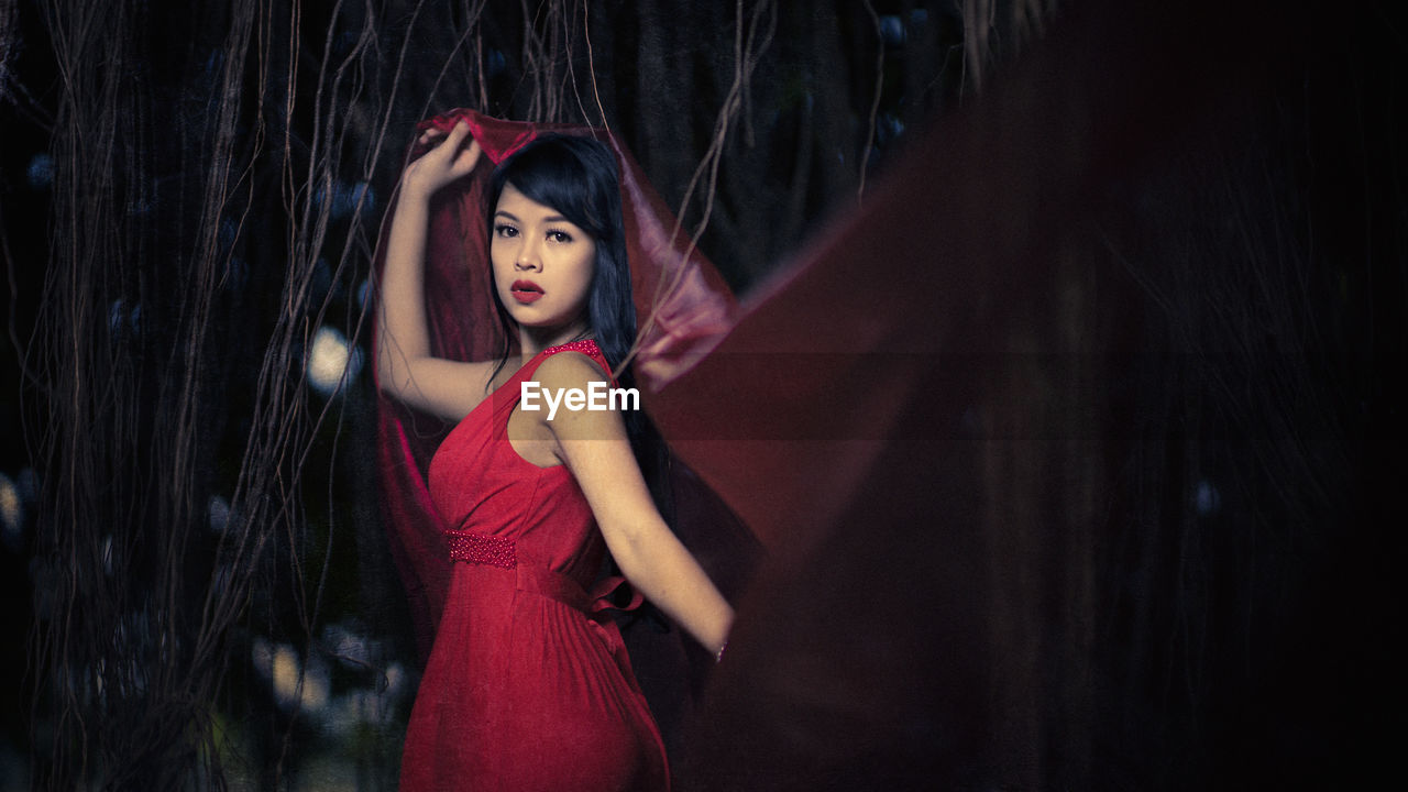 Portrait of young woman wearing red dress while standing in forest