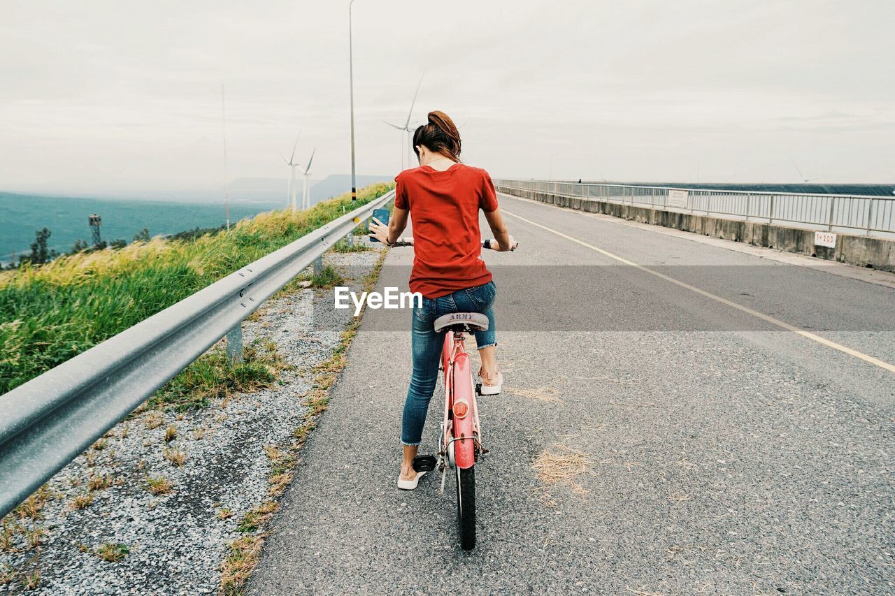 REAR VIEW OF WOMAN RIDING BICYCLE ON ROAD
