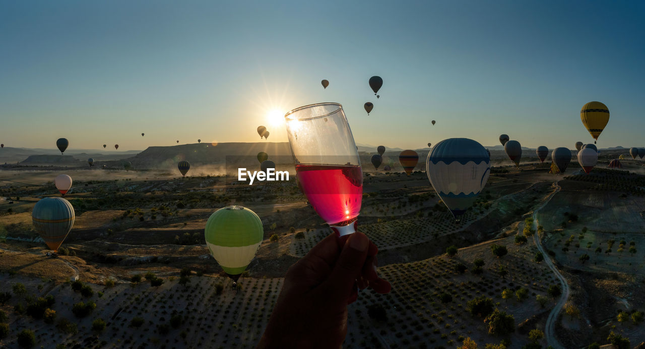 A hand cheers holding a champagne glass with alcohol against hot air balloon flight in cappadocia