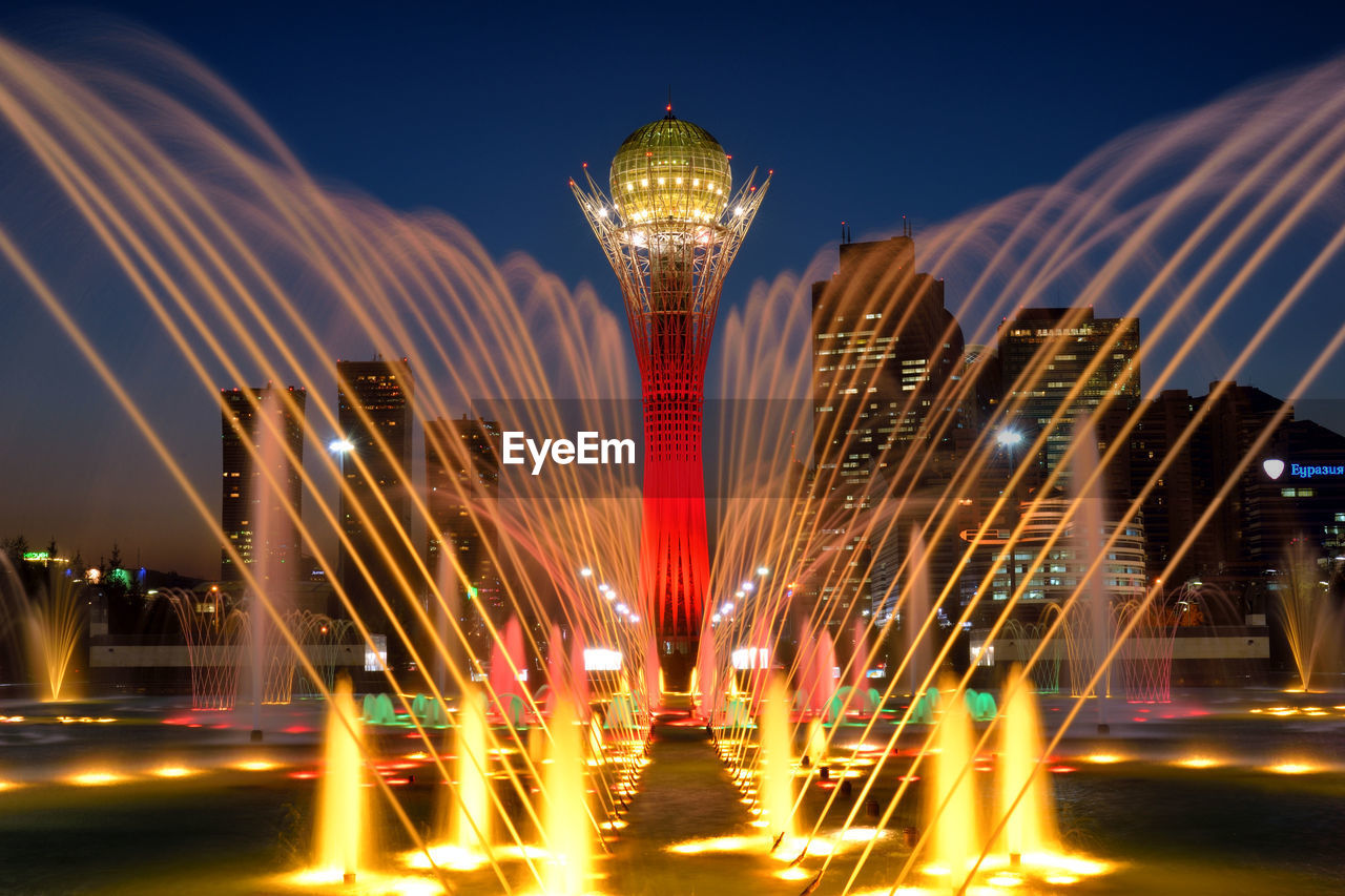 LIGHT TRAILS ON FOUNTAIN AGAINST BUILDINGS AT NIGHT