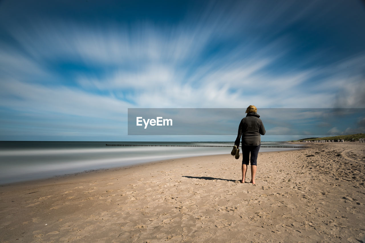 FULL LENGTH REAR VIEW OF WOMAN WALKING ON BEACH AGAINST SKY