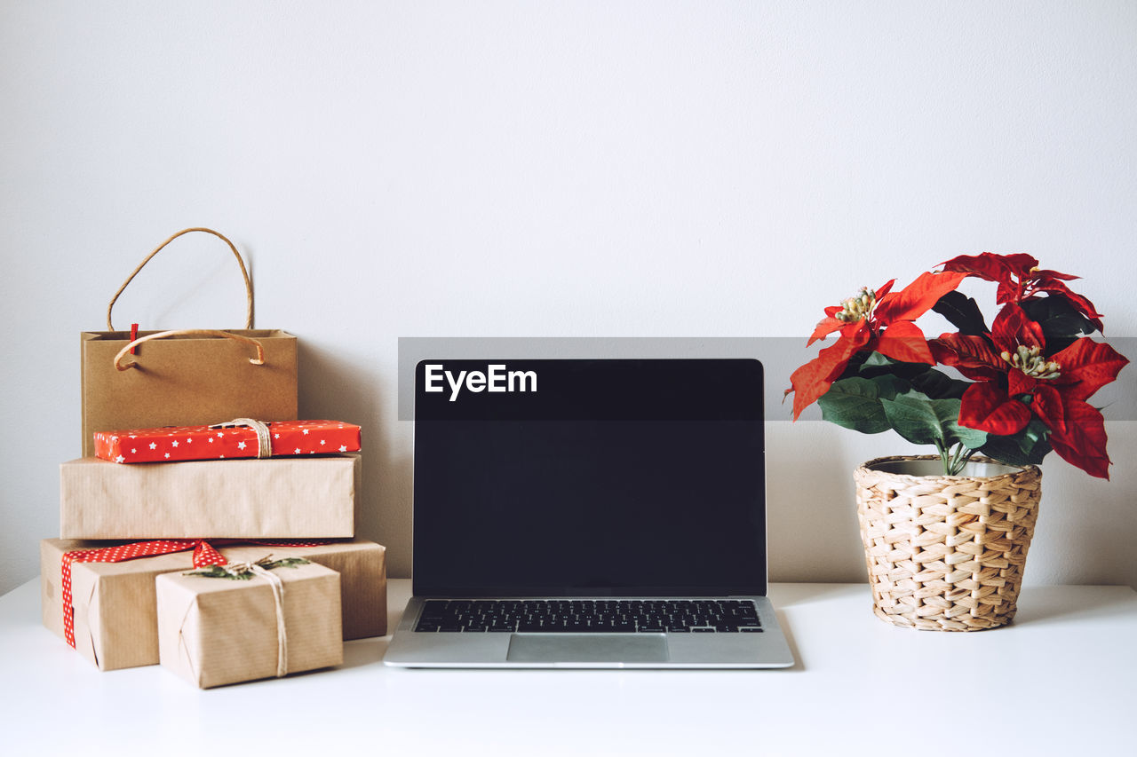 Blank display screen laptop computer with poinsettias christmas flower and gift boxes on white