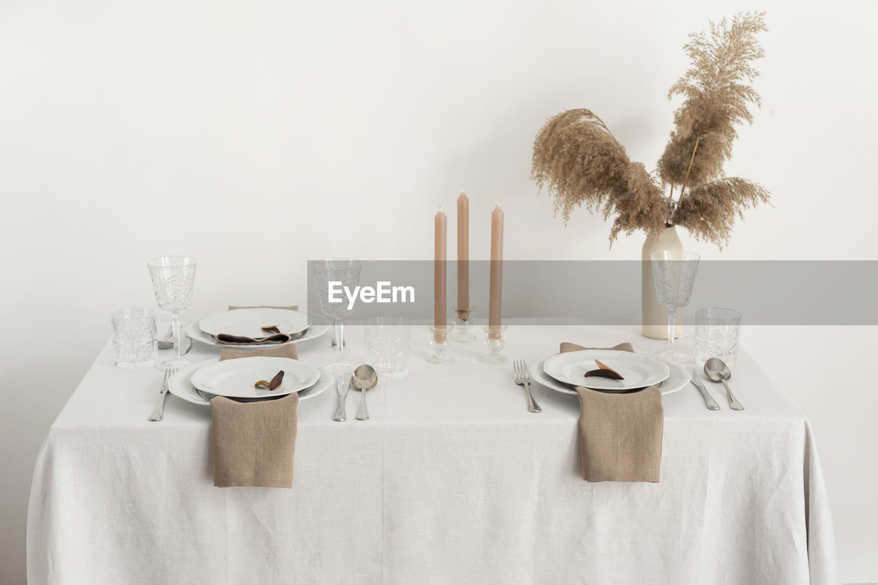 table, setting, tablecloth, indoors, household equipment, place setting, no people, food and drink, furniture, celebration, plant, nature, white, glass, kitchen utensil, eating utensil, napkin, textile, dining table, decoration, drinking glass, fork, elegance, wine glass, home interior, seat, food, copy space, arrangement, plate, crockery, table knife, domestic life, event, knife, still life, chair, studio shot, domestic room