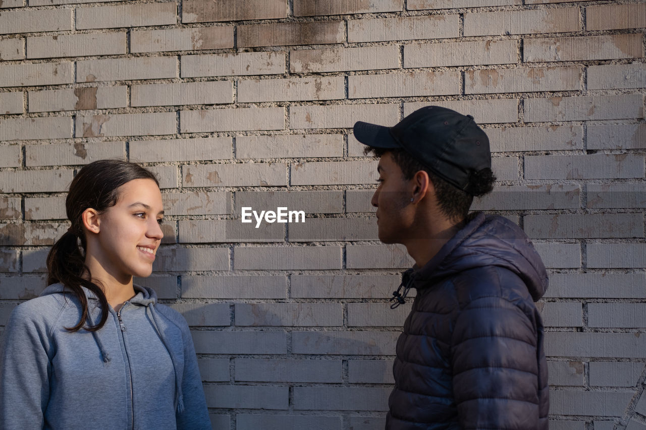 Young couple talking and smiling standing against a brick wall. love signals between teenagers