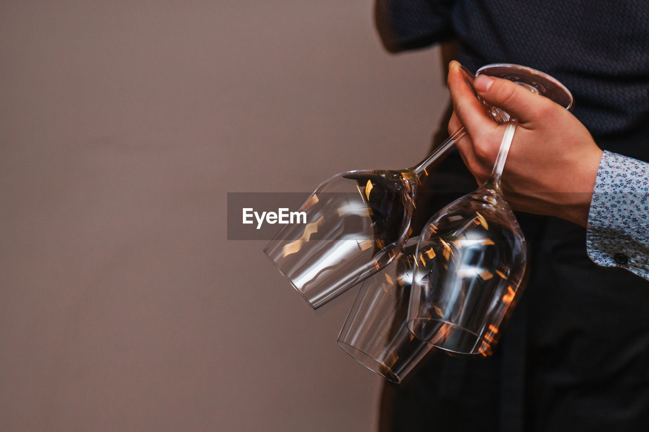 Waiter's hand holding three wine glasses at the same time, light reflections 