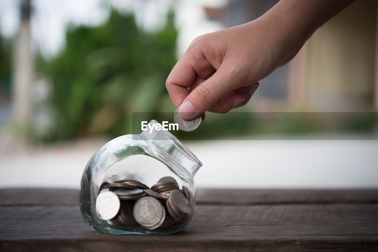 Close-up of person putting coin in jar on table