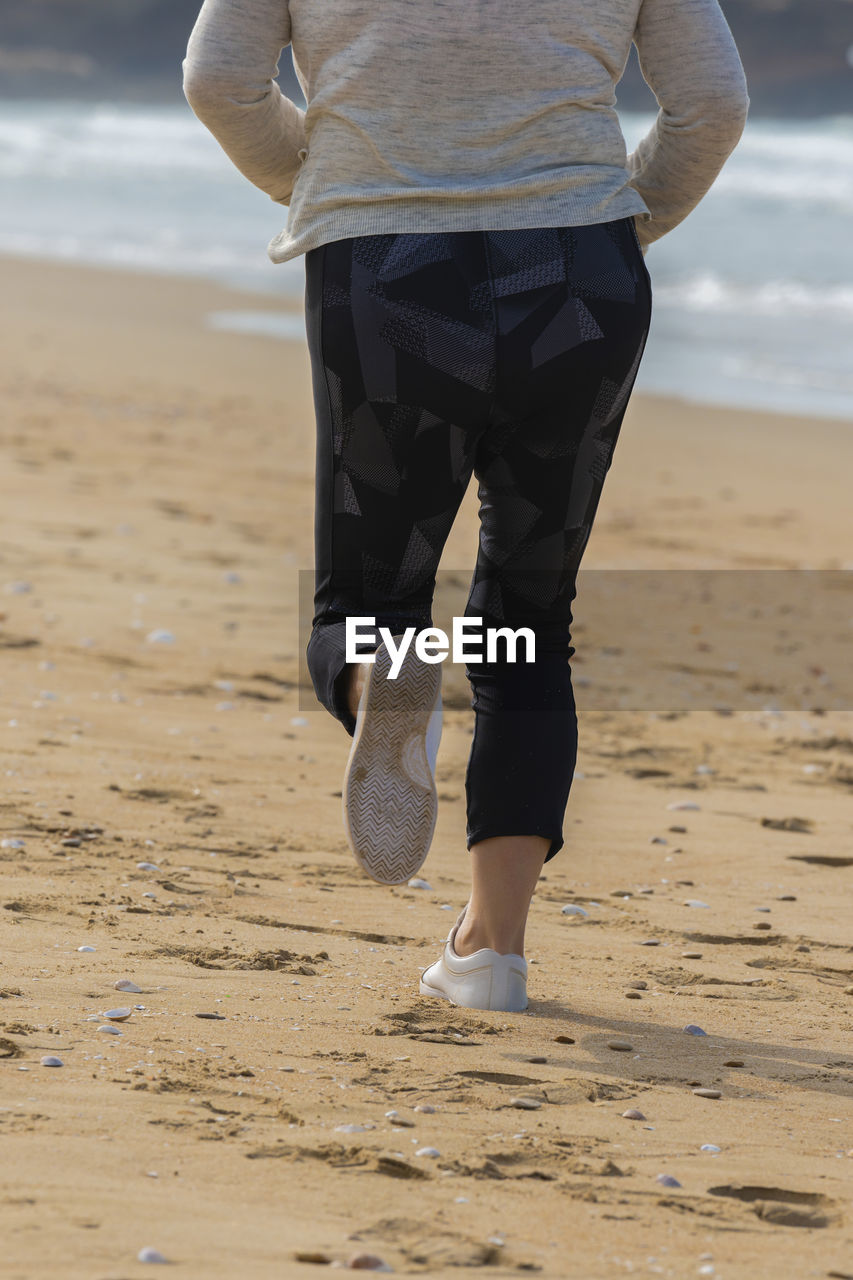 Low section of man walking on beach