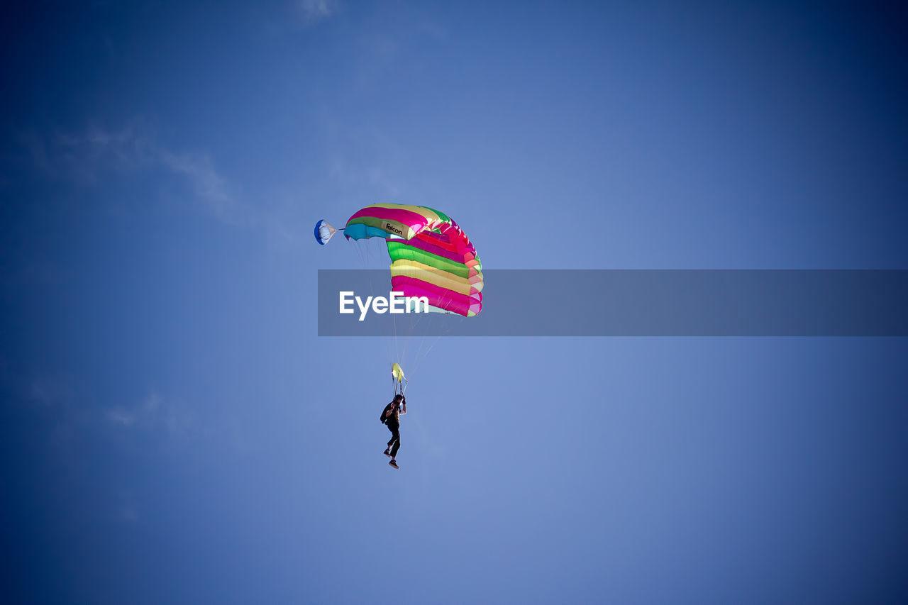 Low angle view of person paragliding against blue sky