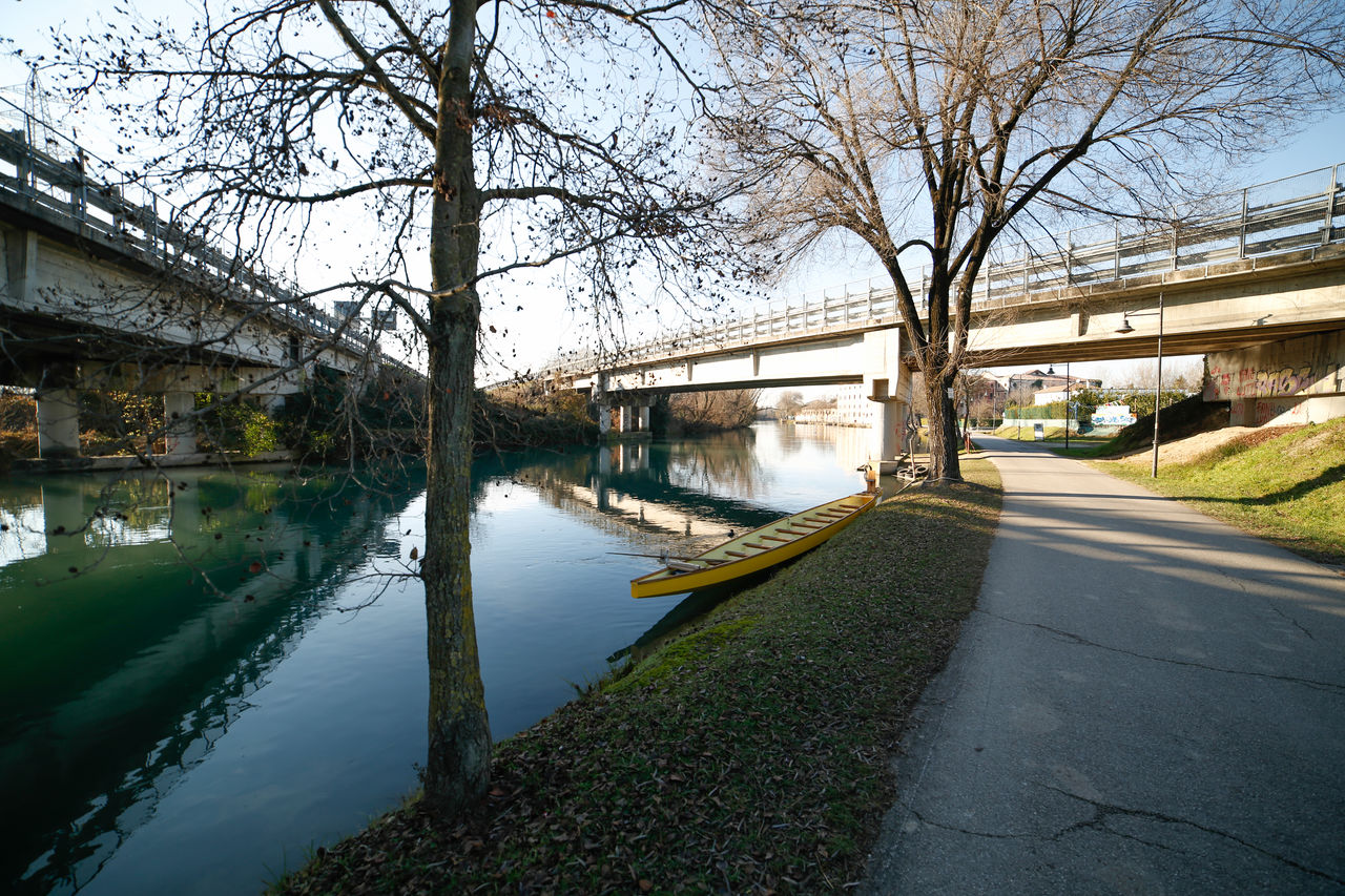 Canal amidst bare trees against sky in city