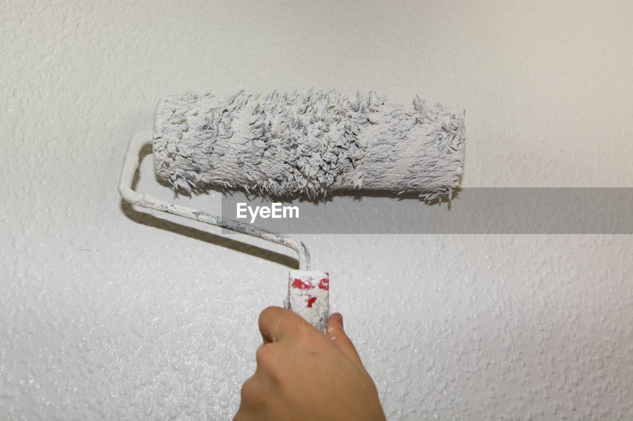 Cropped hand of person holding paint roller against wall