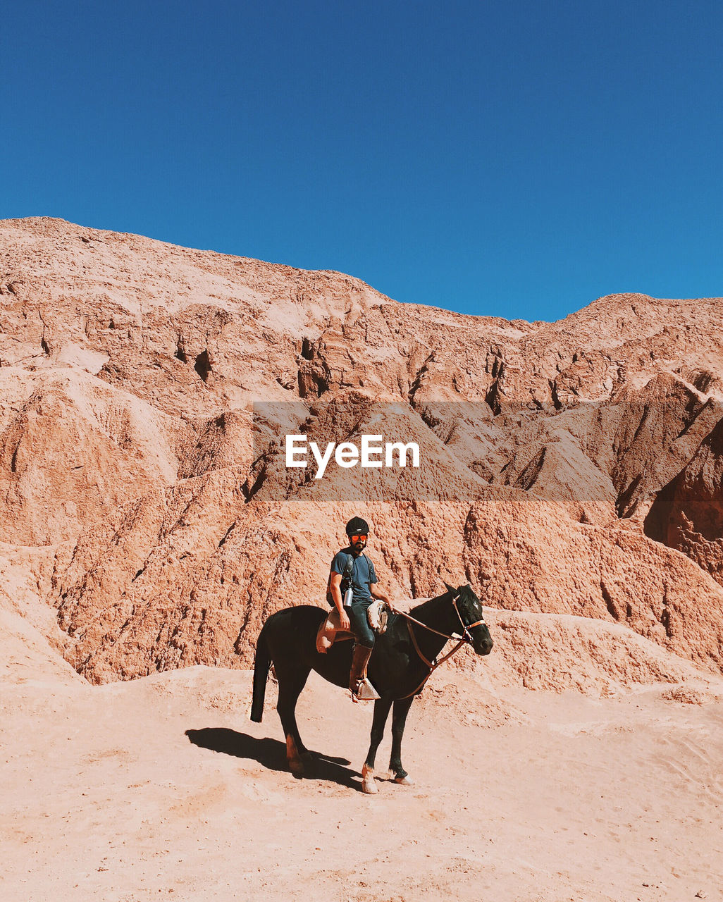 Men riding horse in desert against clear blue sky