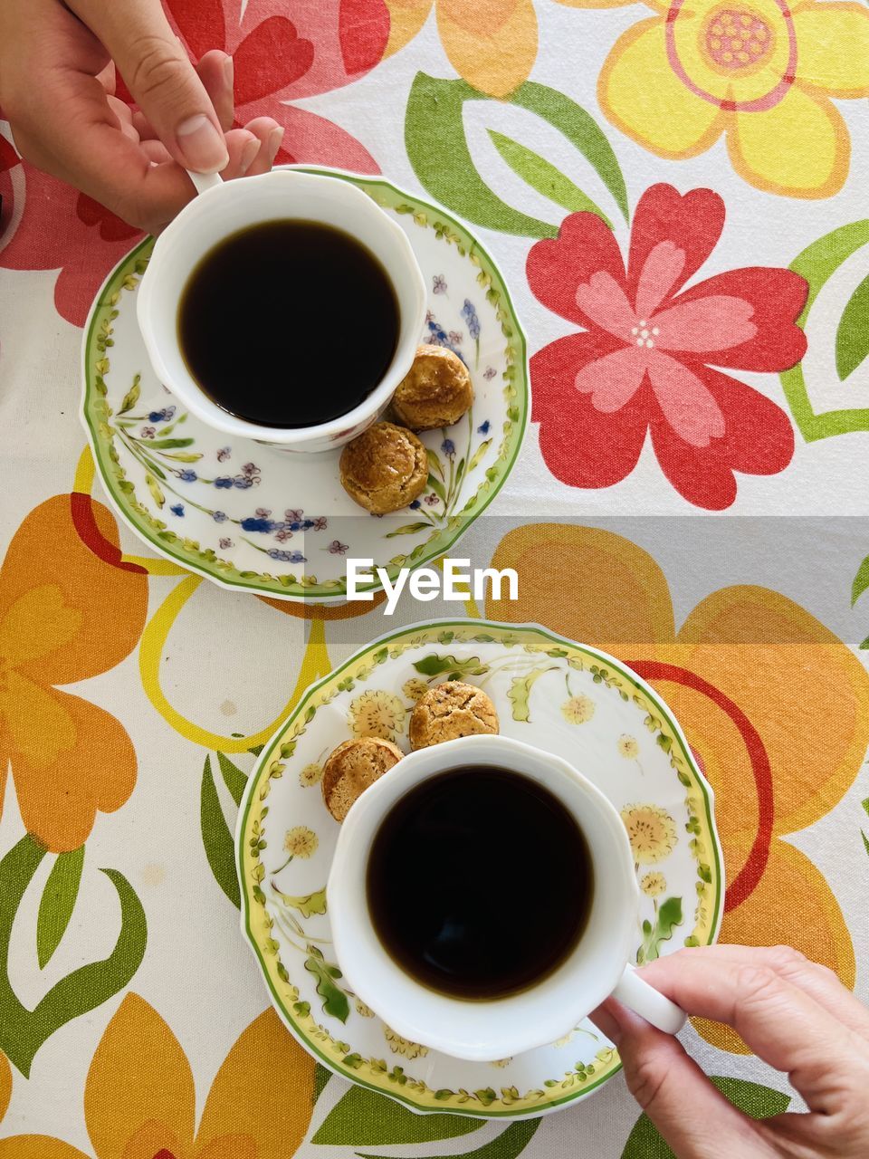 mug, cup, food and drink, drink, hand, coffee, coffee cup, refreshment, crockery, hot drink, one person, tea, food, saucer, table, tea cup, holding, high angle view, pattern, indoors, adult, black coffee, lifestyles, turkish coffee, freshness, floral pattern, leisure activity, directly above, women, breakfast, morning, caffè americano, spoon, meal, flower, kitchen utensil, black tea, eating utensil