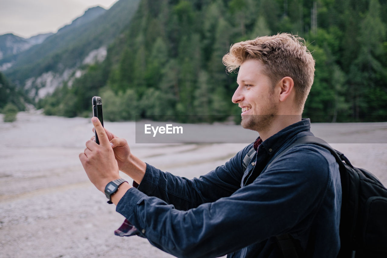 Side view of young man using mobile phone while standing on land