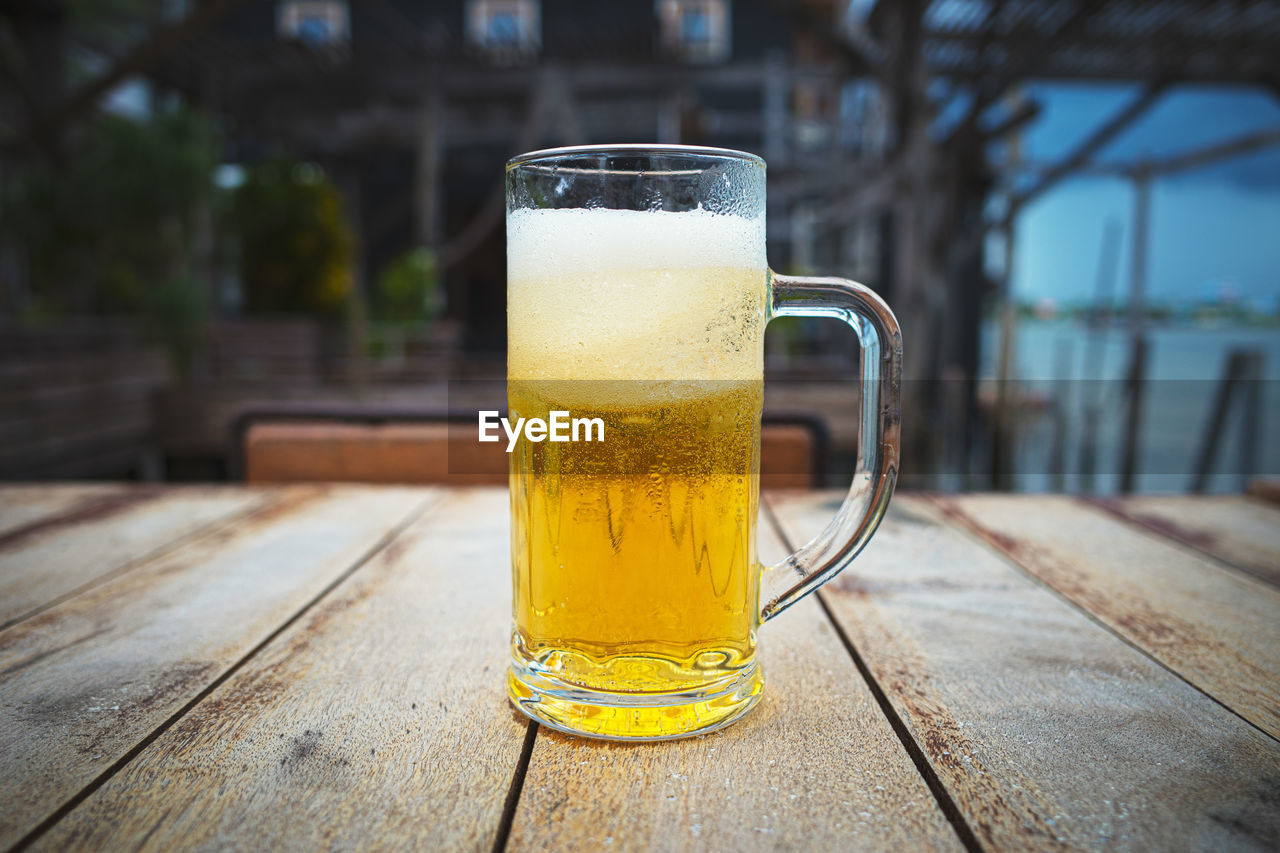 CLOSE-UP OF BEER GLASS ON TABLE AGAINST BLURRED BACKGROUND