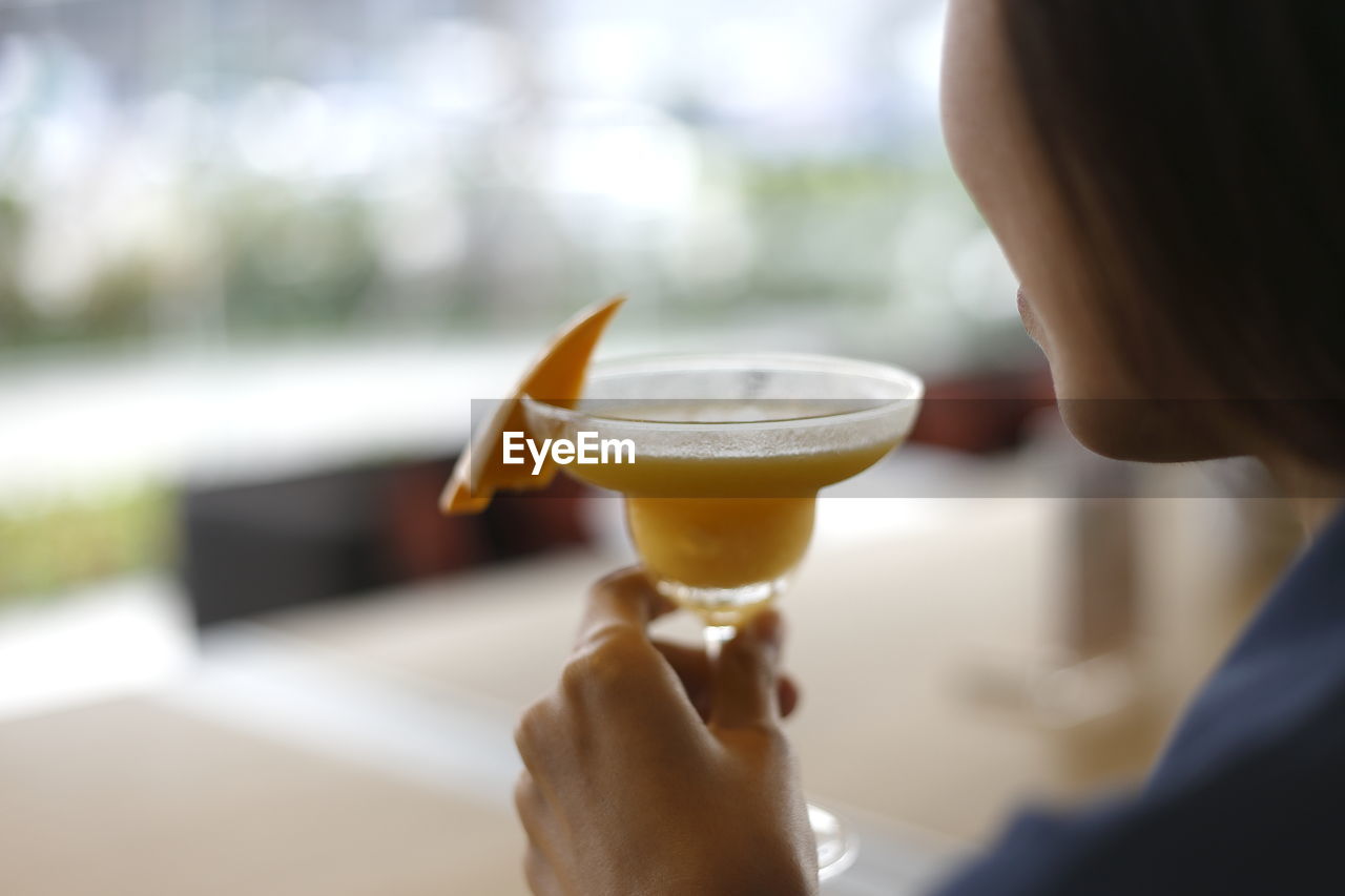 Cropped image of woman having mango smoothie at cafe