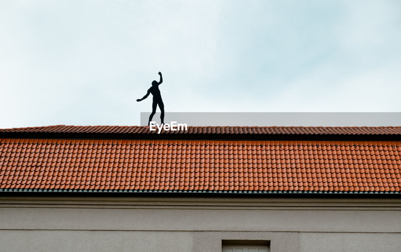 Low angle view of silhouette man on house roof against sky
