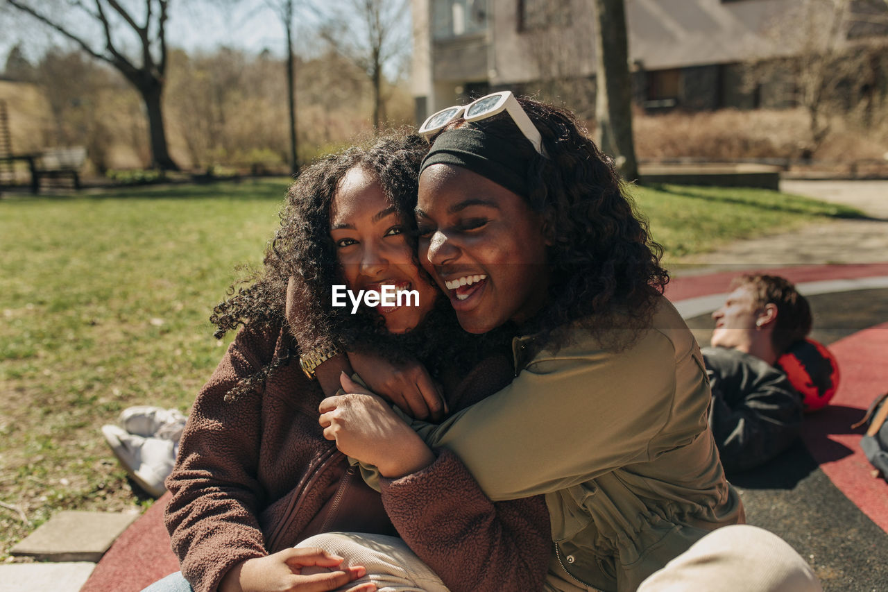 Happy multiracial female friends embracing each other while sitting in playground on sunny day