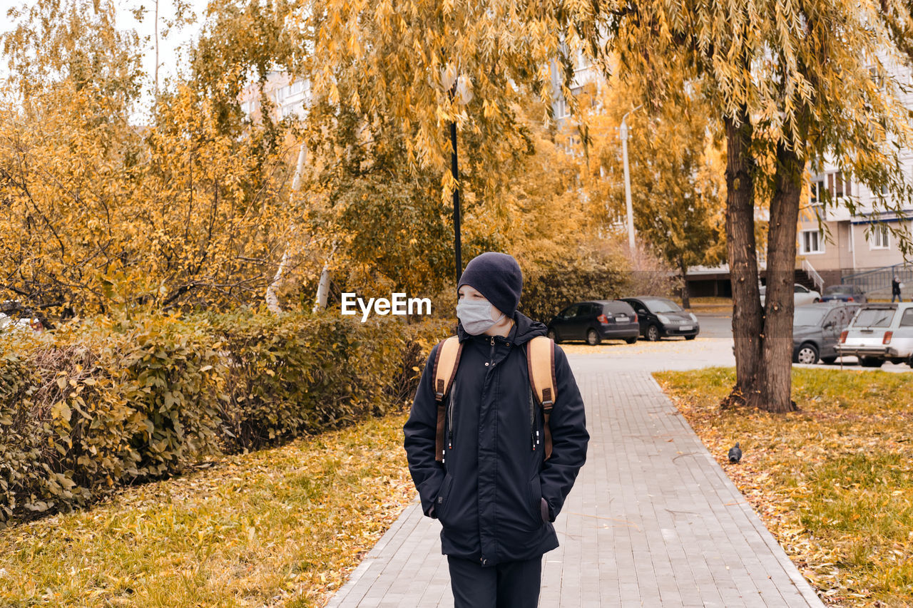 Boy wearing mask standing on footpath during autumn