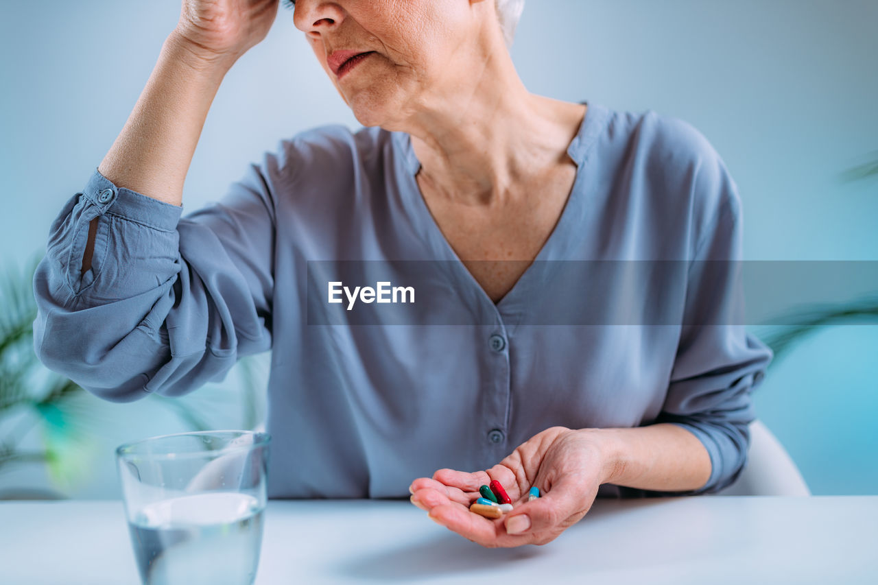 Senior woman with migraine headache holding painkiller pills