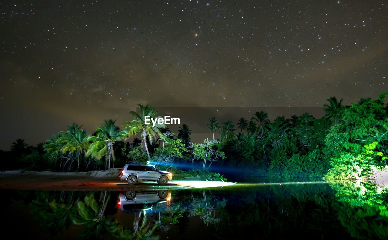 Reflection of car and trees in lake against star field