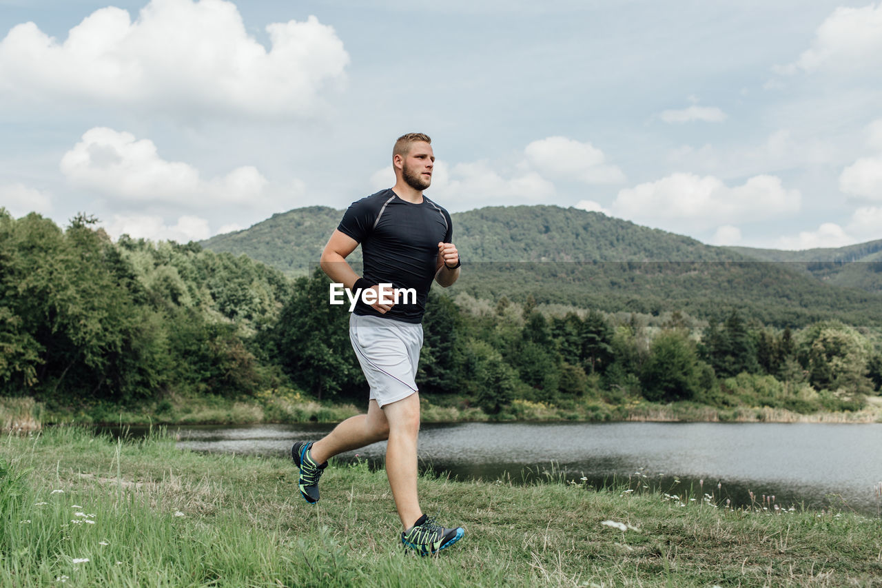 Full length of young man jogging on grassy field by lake